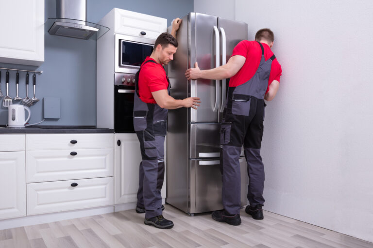 Two Sudan Movers Placing Steel Refrigerator In Kitchen